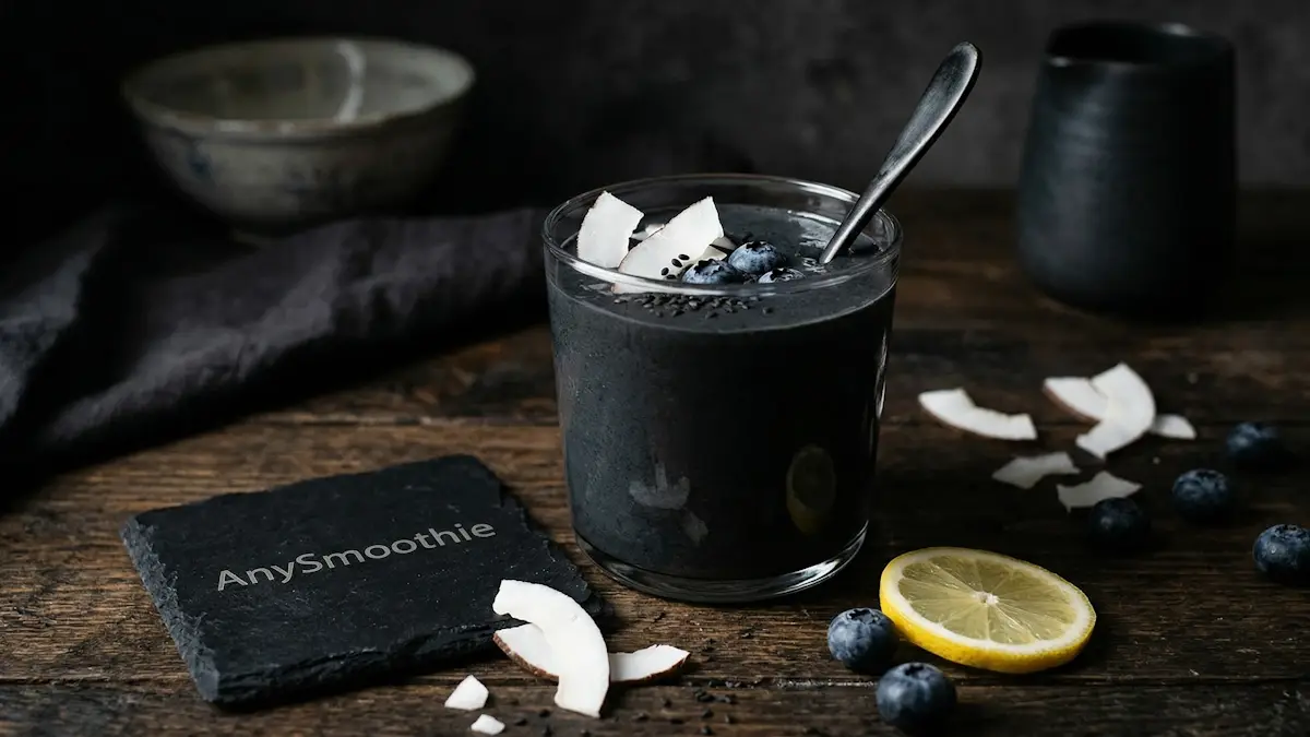 A dramatic jet-black activated charcoal smoothie in a clear glass with white coconut shards and lemon, featuring a black slate coaster with AnySmoothie laser-etched logo.