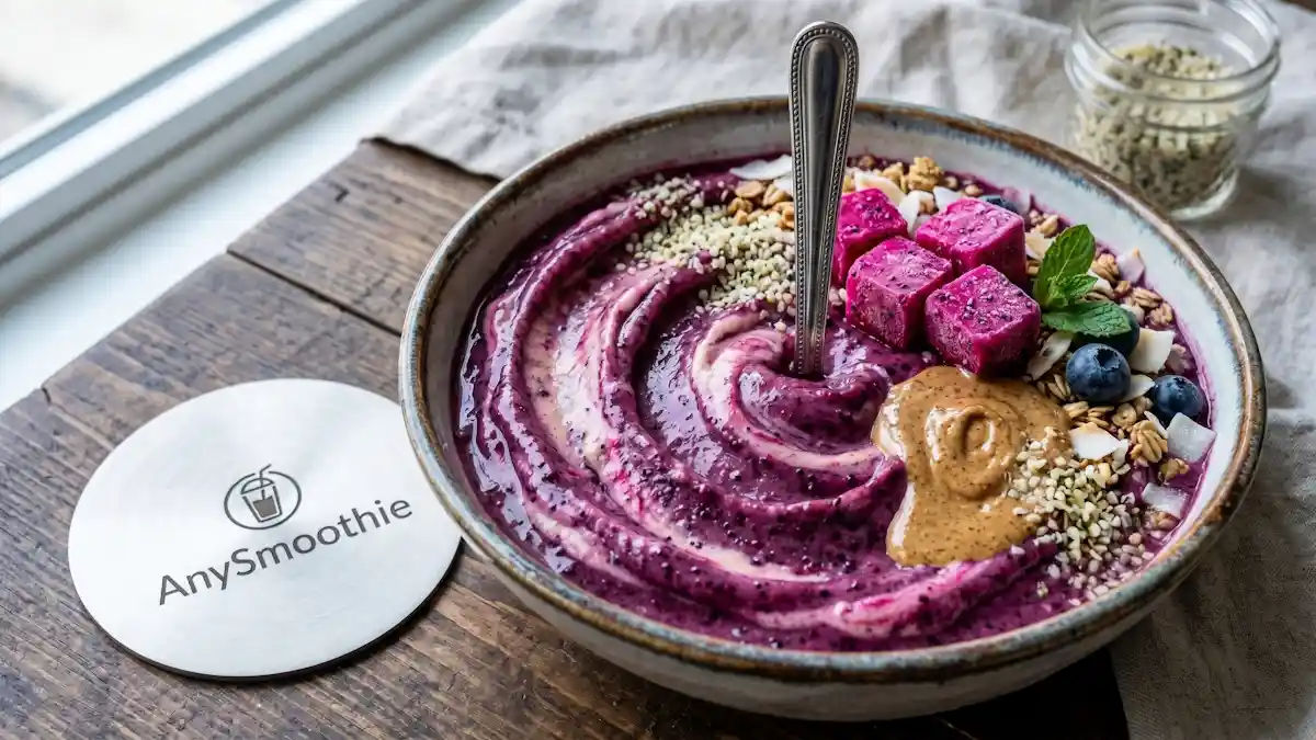 A 4k sharp shot of a thick, swirl-patterned smoothie bowl with a vertical silver spoon, demonstrating structural integrity next to an AnySmoothie laser-etched titanium coaster, featuring frozen dragon fruit cubes and almond butter.